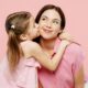 A young girl hugging an adult woman, both wearing pink, against a pink background.