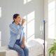 Woman with sterile tube in arm sitting by pole with IV bottle at medical center, drinking water and receiving vitamin therapy infusion to boost body immune system, preserve beauty or fight hangover