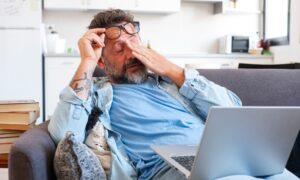 Tired businessman takes off glasses and feels eye strain from working online with laptop, Caucasian man sits on sofa and rubs his eyes, feels headache and lack of energy