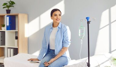 Young happy smiling woman sitting on the couch in medical clinic looking at the window while receiving IV drip infusion and vitamin injection therapy in her blood. Healthcare concept.