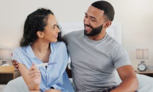 Happy couple, pregnancy stick and results in home, hug and support for positive baby news. People, plastic test and together for reading ovulation tool in bedroom, fertility treatment and embrace