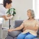 Senior woman with intravenous drip sitting on couch, physician, nurse doctor fixing IV drip infusion, geriatrics hospital eldercare, therapy to infuse vitamins, chemotherapy to maintain health clinic