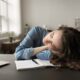 Drained young student woman sleeping, dozing lying down on desk, overloaded with studying, exams preparation, feels lack of energy after sleepless working night. Low productivity, overworking, fatigue