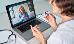 Female doctor therapist consulting older senior patient via virtual video call visit using laptop computer. Digital online healthcare, distance telemedicine. Telehealth videocall. Over shoulder view
