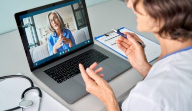 Female doctor therapist consulting older senior patient via virtual video call visit using laptop computer. Digital online healthcare, distance telemedicine. Telehealth videocall. Over shoulder view