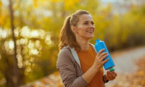 Hello autumn. happy trendy middle aged woman in fitness clothes in the park with bottle of water.