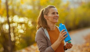 Hello autumn. happy trendy middle aged woman in fitness clothes in the park with bottle of water.