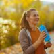 Hello autumn. happy trendy middle aged woman in fitness clothes in the park with bottle of water.