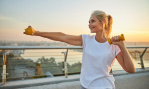 Smiling attractive energetic sporty blonde Caucasian female athlete boxing with dumbbells on a pedestrian bridge