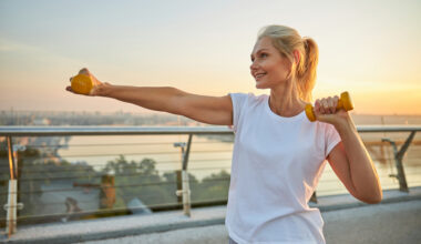 Smiling attractive energetic sporty blonde Caucasian female athlete boxing with dumbbells on a pedestrian bridge