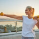 Smiling attractive energetic sporty blonde Caucasian female athlete boxing with dumbbells on a pedestrian bridge