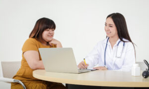 Smiling physician consulting with a patient while taking notes on a laptop, representing a supportive liraglutide doctor visit.