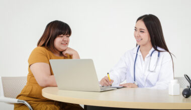 Smiling physician consulting with a patient while taking notes on a laptop, representing a supportive liraglutide doctor visit.