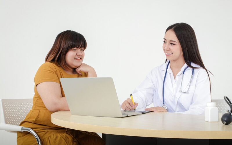 Smiling physician consulting with a patient while taking notes on a laptop, representing a supportive liraglutide doctor visit.