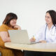 Smiling physician consulting with a patient while taking notes on a laptop, representing a supportive liraglutide doctor visit.