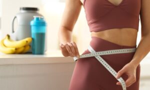 Weight loss. Woman measuring waist with tape in kitchen, closeup