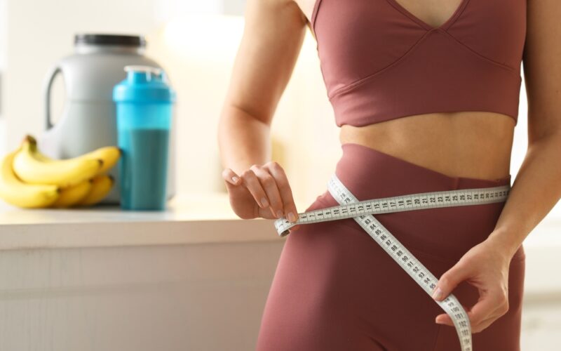 Weight loss. Woman measuring waist with tape in kitchen, closeup