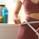 Weight loss. Woman measuring waist with tape in kitchen, closeup