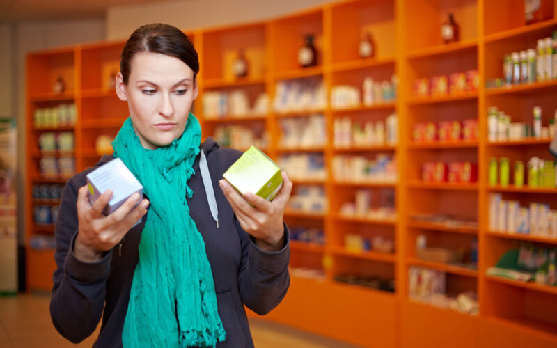 Woman in a pharmacy comparing two medication boxes, symbolizing patient decisions when choosing between semaglutide and liraglutide