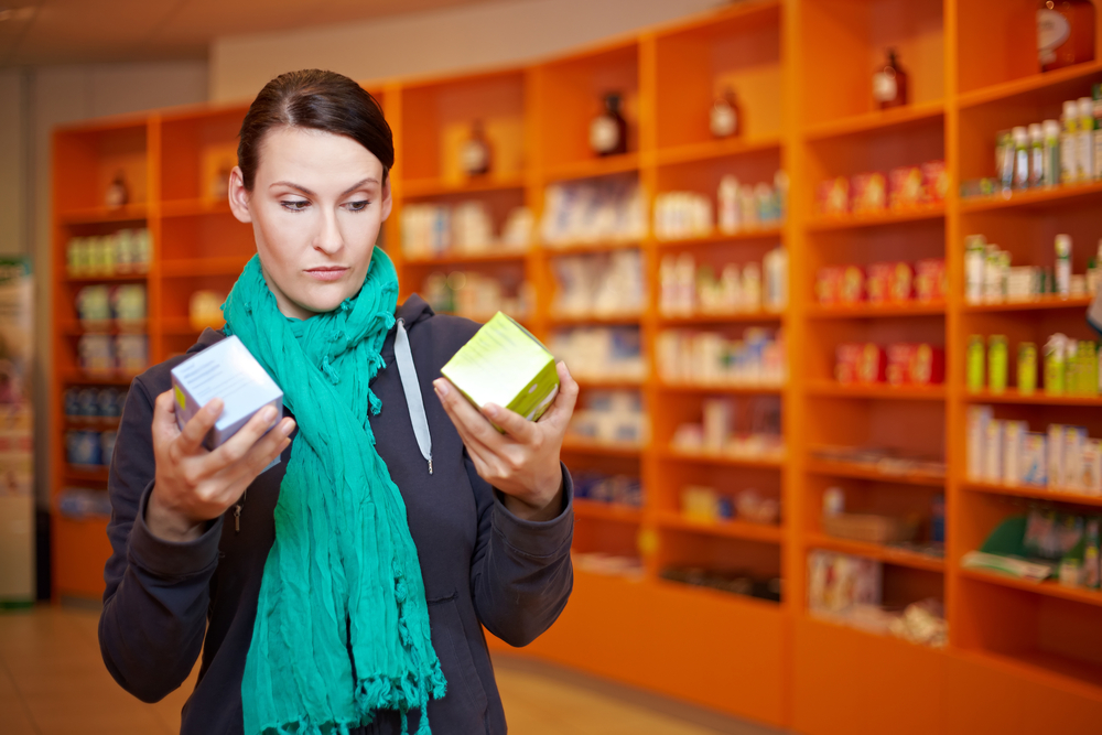 Woman in a pharmacy comparing two medication boxes, symbolizing patient decisions when choosing between semaglutide and liraglutide