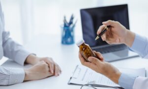 Doctor holding a pill bottle while consulting with a patient, discussing treatment options and differences between liraglutide and semaglutide.