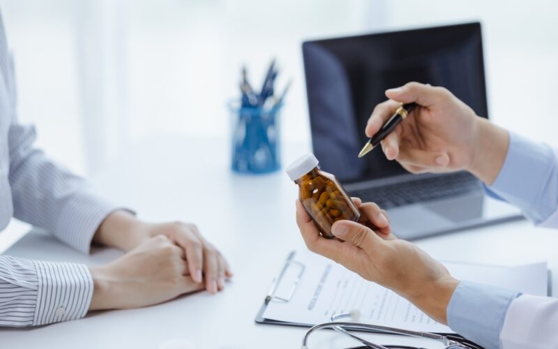 Doctor holding a pill bottle while consulting with a patient, discussing treatment options and differences between liraglutide and semaglutide.
