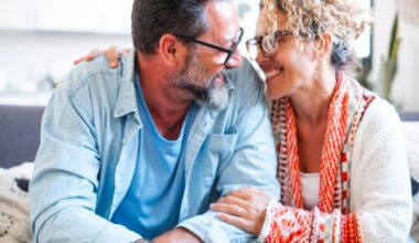 An adult couple in their late 40s, wearing glasses, smiling and embracing each other