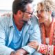 An adult couple in their late 40s, wearing glasses, smiling and embracing each other