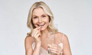Happy middle aged 50s woman holding pill and glass of water taking dietary supplements
