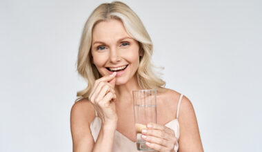 Happy middle aged 50s woman holding pill and glass of water taking dietary supplements