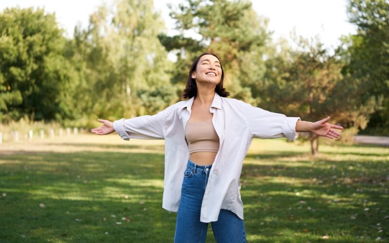 Happy woman standing outdoors with open arms and eyes closed, enjoying fresh air and sunlight — representing freedom, confidence, and the positive results of a successful semaglutide weight loss journey.