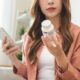 Health care asian young woman using smart phone for reading, searching prescription on bottle medicine, pill label text about information online, instructions side effects, pharmacy medicament concept