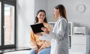 medicine, healthcare and people concept - female doctor with tablet pc computer talking to smiling woman patient at hospital