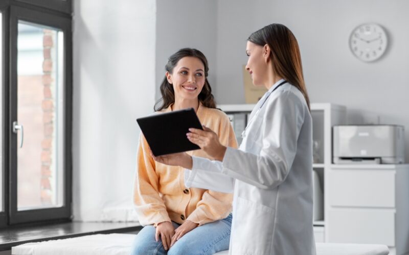 medicine, healthcare and people concept - female doctor with tablet pc computer talking to smiling woman patient at hospital