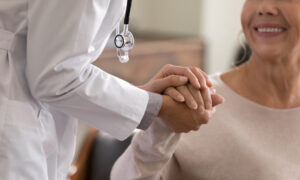 Doctor giving hope. Close up shot of young female physician leaning forward to smiling elderly lady patient holding her hand in palms. Woman caretaker in white coat supporting encouraging old person. How to talk to your doctor about perimenopause symptoms and treatment goals