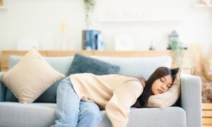 Asian woman resting at home on couch, feeling exhausted after work, lacking energy, or overworked, too tired, and lacking motivation
