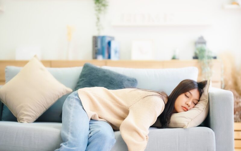 Asian woman resting at home on couch, feeling exhausted after work, lacking energy, or overworked, too tired, and lacking motivation