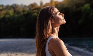 Young woman with long hair enjoying sun with closed eyes getting natural vitamin D outdoors. Peace of mind. Mindfulness, mental health, spirituality, well-being, unwind yourself. Sermorelin Dosage