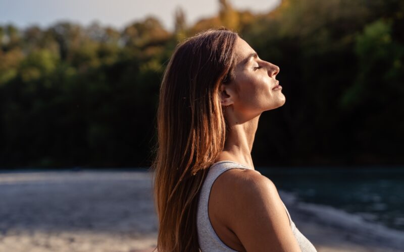 Young woman with long hair enjoying sun with closed eyes getting natural vitamin D outdoors. Peace of mind. Mindfulness, mental health, spirituality, well-being, unwind yourself. Sermorelin Dosage
