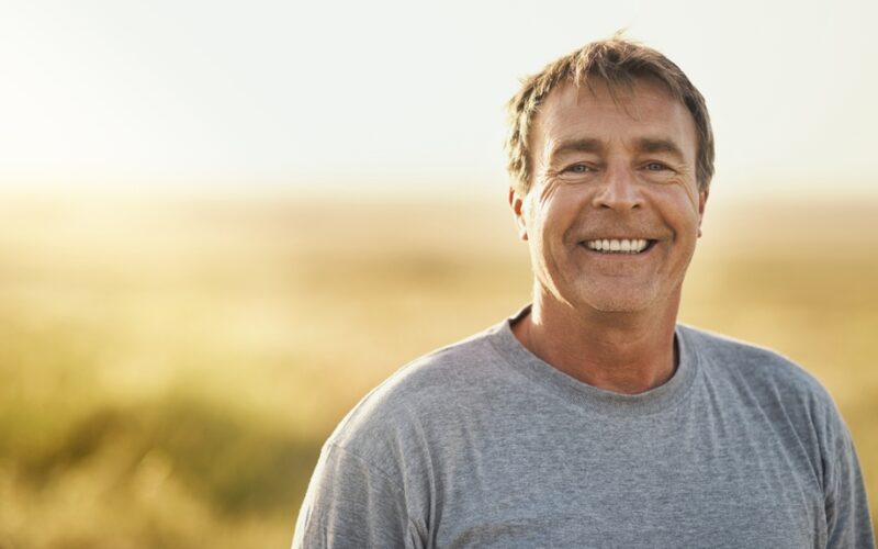 Senior man, smile and portrait at field in summer for outdoor adventure, nature and holiday. Sunshine, happy and face of person by mockup space for weekend vacation, peace and tourism in Turkey