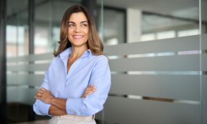 Happy confident mature professional business woman standing at work in office arms crossed looking away, proud hispanic middle aged businesswoman leader executive thinking of future success. Sermorelin for women: hormone balance, sleep, and skin health.