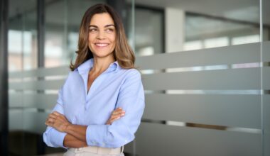 Happy confident mature professional business woman standing at work in office arms crossed looking away, proud hispanic middle aged businesswoman leader executive thinking of future success. Sermorelin for women: hormone balance, sleep, and skin health.