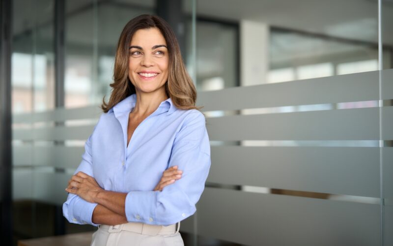 Happy confident mature professional business woman standing at work in office arms crossed looking away, proud hispanic middle aged businesswoman leader executive thinking of future success. Sermorelin for women: hormone balance, sleep, and skin health.