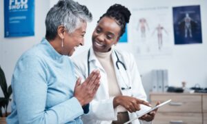 Black woman, doctor and elderly patient with good news, tablet and results for health, advice and report. Happy african medic, mobile touchscreen or healthcare with smile, tech or support in hospital