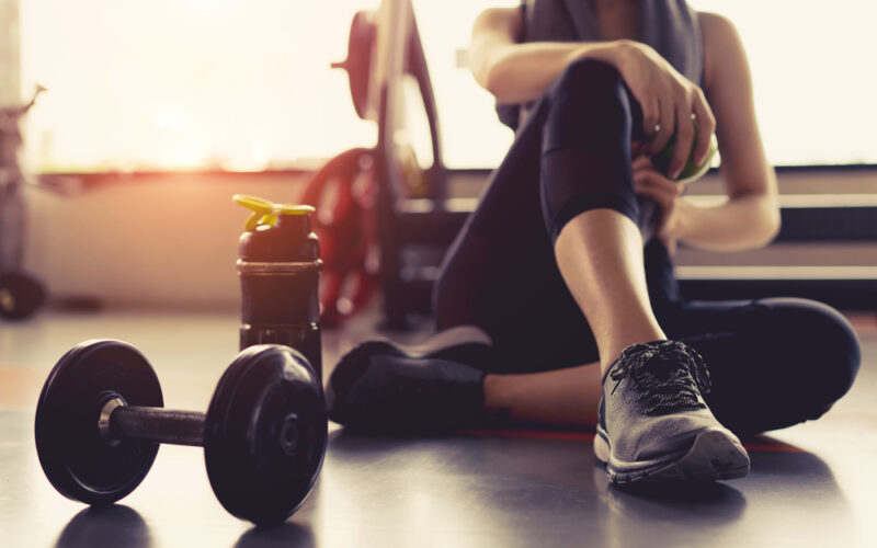 Woman tirzepatide exercise workout in gym fitness breaking relax holding apple fruit after training sport with dumbbell and protein shake bottle healthy lifestyle bodybuilding, Athlete builder muscles lifestyle.