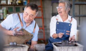 An older couple smiling and laughing while working with clay at a pottery wheel, symbolizing creativity, vitality, and healthy aging supported by NAD+ therapy.
