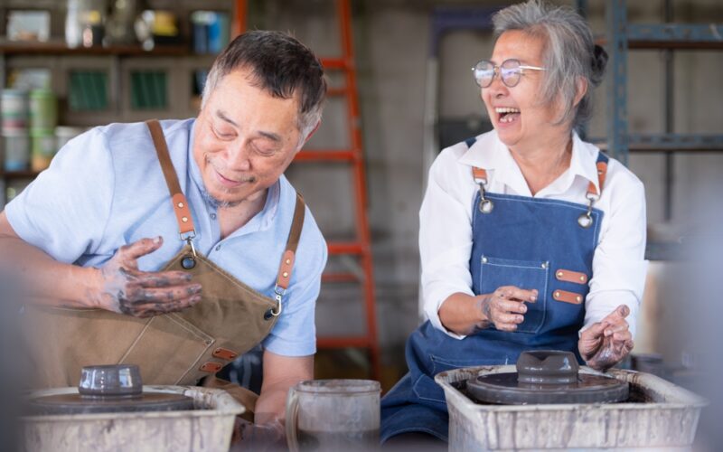 An older couple smiling and laughing while working with clay at a pottery wheel, symbolizing creativity, vitality, and healthy aging supported by NAD+ therapy.