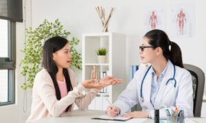 A woman talks openly with her female doctor during a medical consultation in a bright office. The doctor, wearing a white coat and stethoscope, listens attentively and takes notes, symbolizing supportive care for sensitive health concerns.