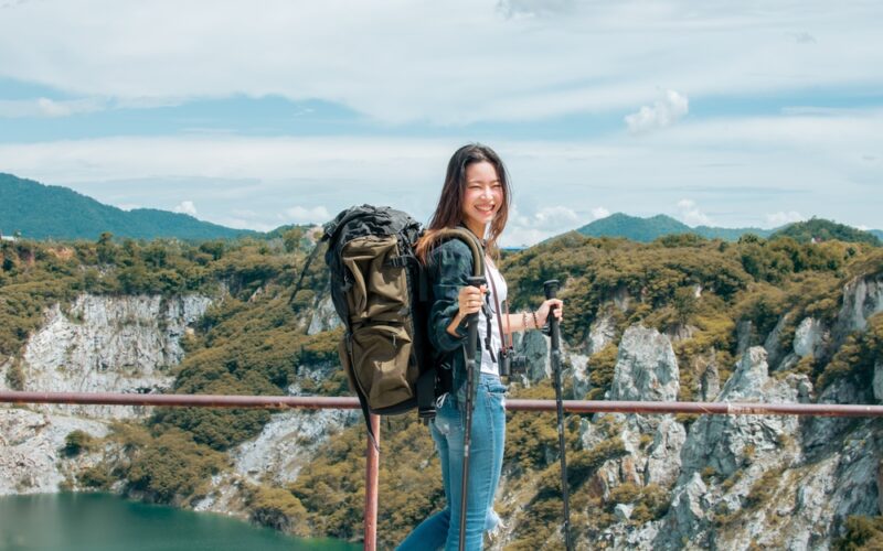Smiling woman with a large hiking backpack and trekking poles standing on a scenic overlook, representing the role of active lifestyle choices in supporting tirzepatide’s effectiveness for weight management.