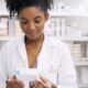 Tirzepatide Woman, pharmacist and checking box with medication, side effects or symptoms at pharmacy. Young African, female person or medical employee reading expiry date on pharmaceutical product at store
